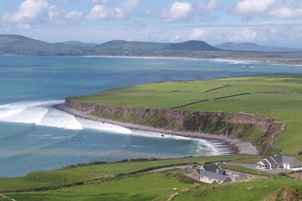Green cliffs over a blue bay, white houses, Atlantic waves near Dingle