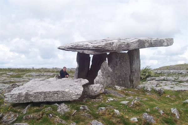 Man sitting beside Poulnabrone dolmen, limestone slabs among green grass