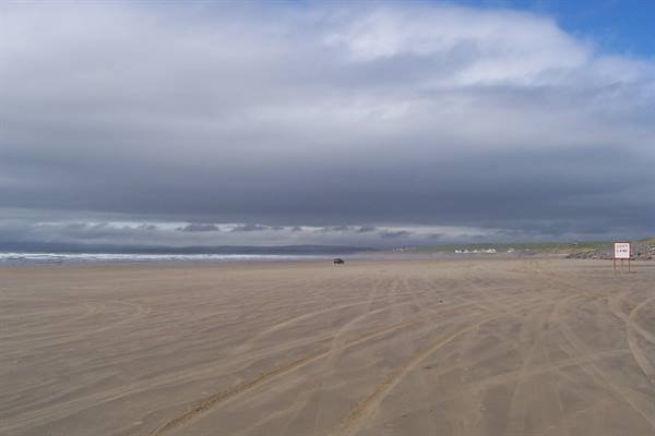 Car on sandy beach with tire tracks, cloudy sky over the ocean