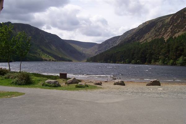 Glendalough lake framed by green mountains and woods under cloudy sky