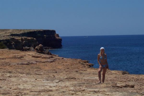 Woman in bikini on rocky cliffs by the blue sea