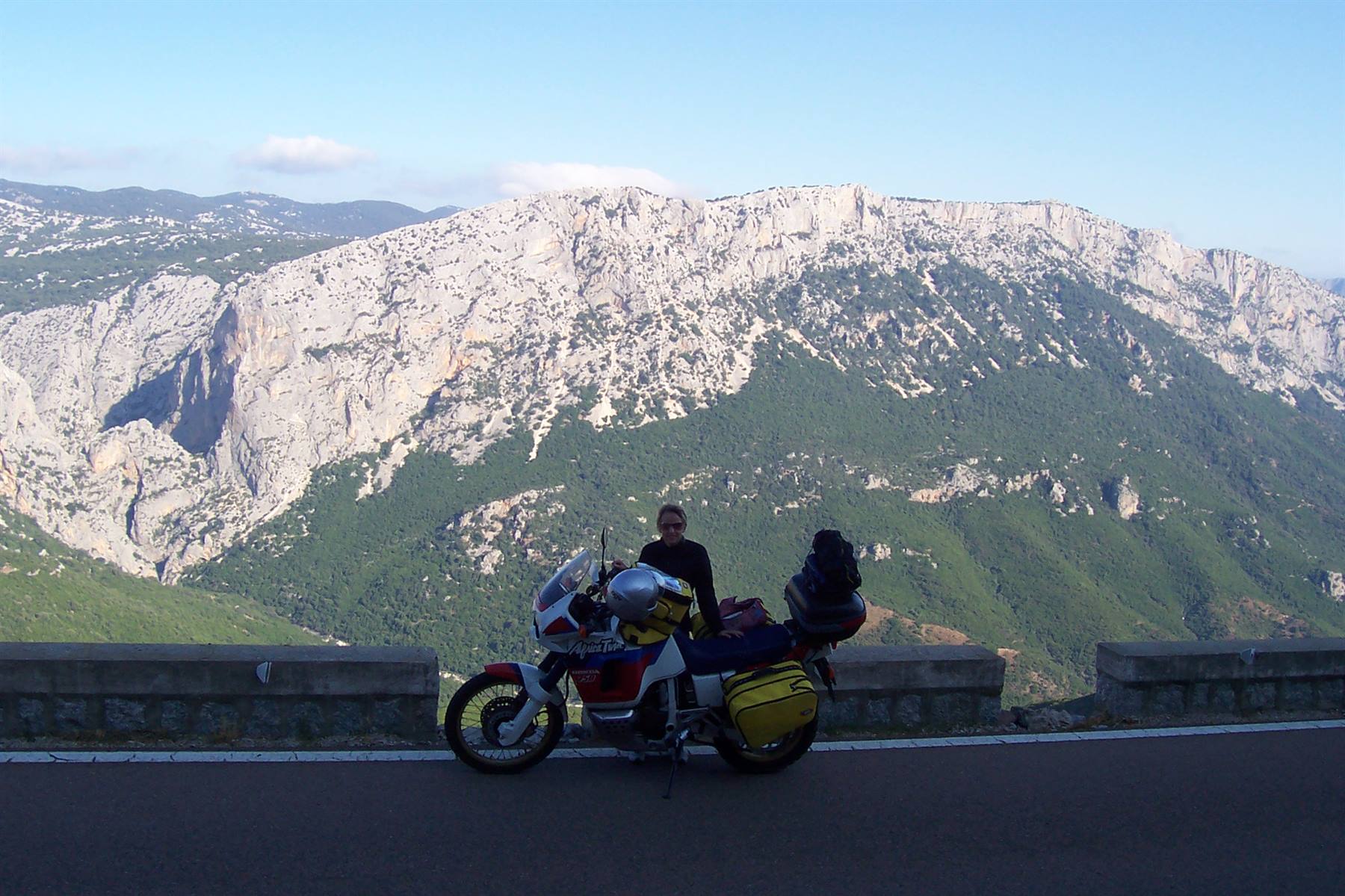 Motorcyclist on a loaded adventure bike in front of rocky limestone mountains