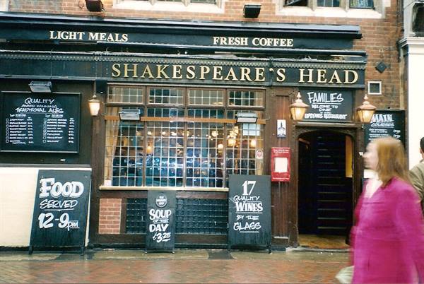  Woman in pink walks past Shakespeare's Head pub, golden sign and blackboards