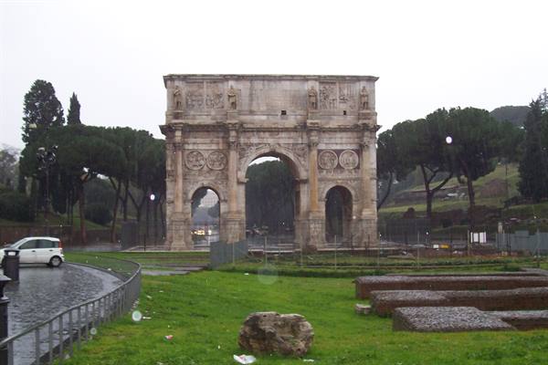Arch of Constantine in Rome under the rain, with lawn and pines