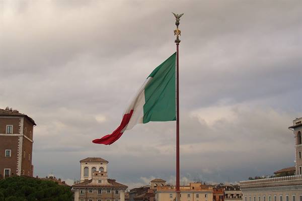 Italian flag waving on a tall pole above Rome's historic rooftops
