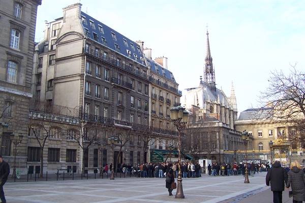 Visitors queue on the Notre-Dame parvis beside Haussmann buildings and street lamps