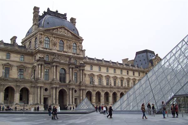 Tourists walk in the Louvre courtyard beside the glass pyramid
