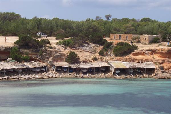 Old wooden boat shelters on the shore, turquoise water, pines and stone houses