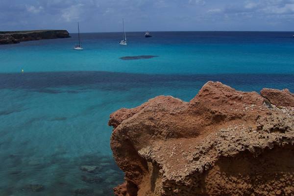Reddish rock over turquoise water, sailboats anchored near the coast