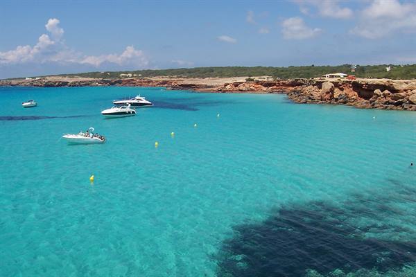 Boats anchored in turquoise water by the red rocks of Cala Saona
