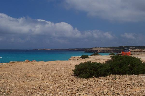 Red van parked on limestone rocks, turquoise sea beneath white clouds