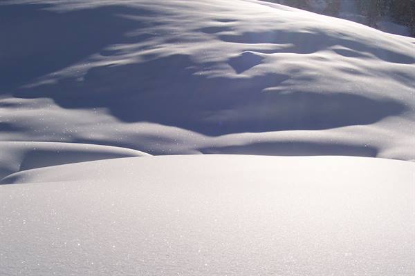 Wind-sculpted compact snow, sunlight glinting on white undulating drifts