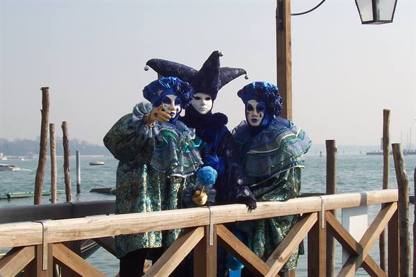 Three blue Venice Carnival masks lean on a wooden walkway by the lagoon