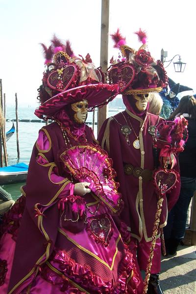 Couple in pink and burgundy costumes with golden masks at Venice Carnival