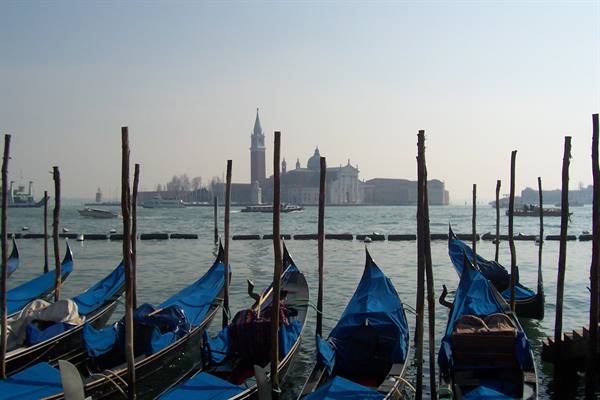 Blue-covered gondolas moored in Venice, San Giorgio Maggiore visible in the haze