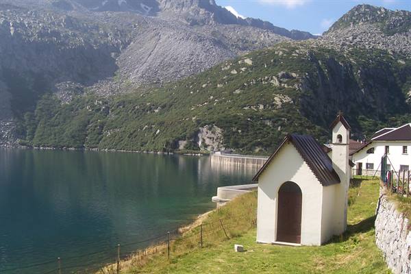 White stone chapel on grassy shore of Robiei lake, dam among mountains