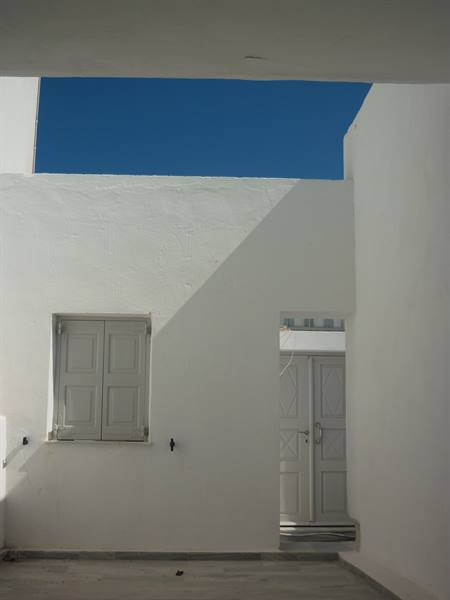 Whitewashed walls with grey shutter and door under deep blue sky
