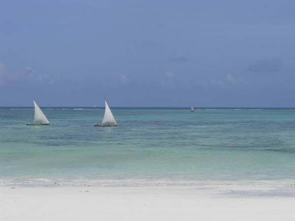 Two white sailboats on turquoise sea in front of white sand beach