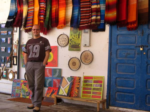 Man smiling in front of colorful rug stall and paintings, blue door