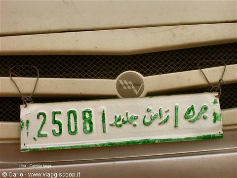 Hand-painted green plate with Arabic writing, wired onto an old truck's grille