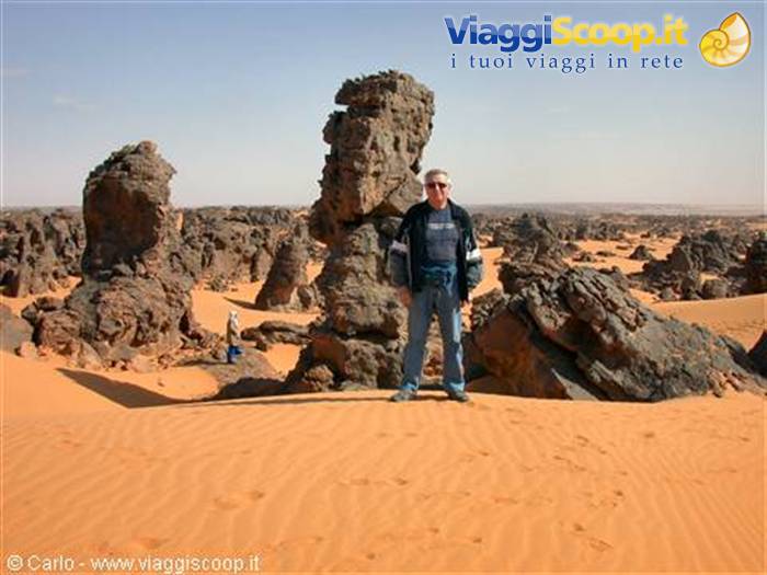 Man standing on sand dune beside eroded volcanic rocks in the Sahara