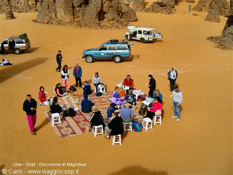 Tourists lunching on carpet among sandy desert rocks in Ghat