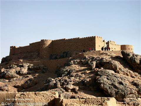 Ancient mud-brick fortress atop a rocky arid hill, tourists on top