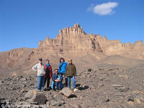 Five tourists posing among rocks in front of desert rocky mountain, blue sky