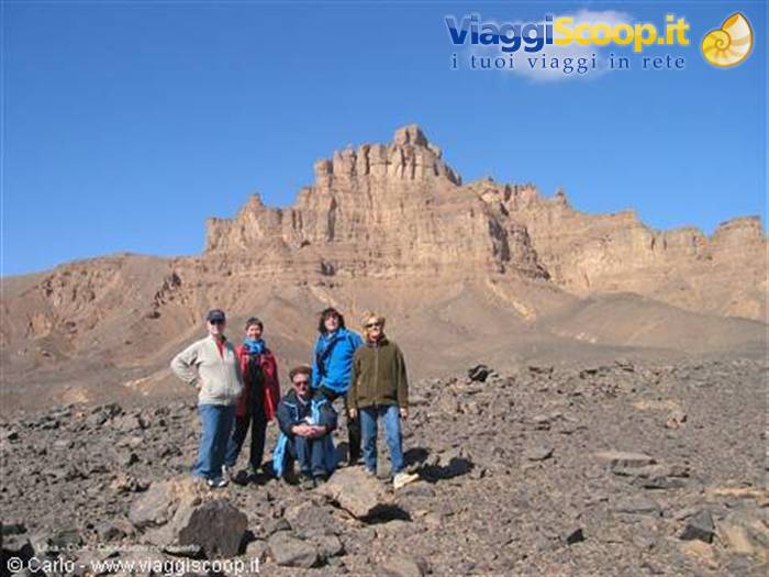 Five tourists posing among rocks in front of desert rocky mountain, blue sky