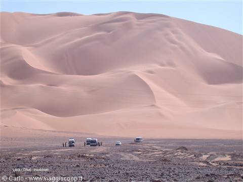 Pink Namib dunes with parked 4x4s and travelers on gravel