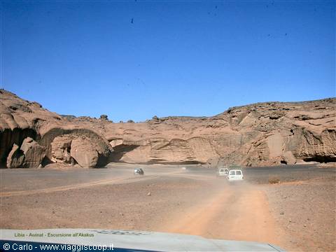 White off-road vehicle raising dust among sandstone cliffs, Akakus