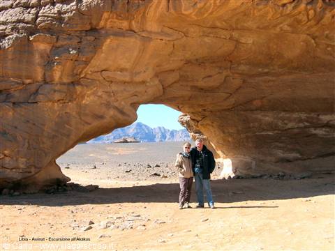 Couple standing beneath a huge natural sandstone arch in the Akakus, Libya