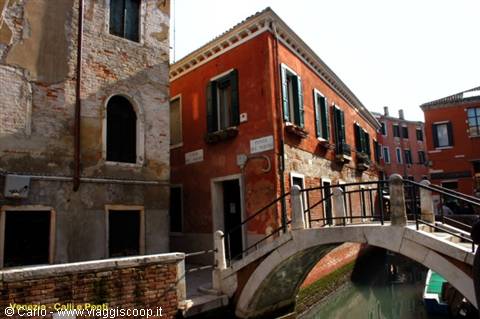 Venice, stone footbridge over a narrow canal between red houses