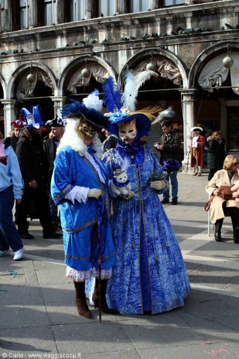 Two figures in blue costumes with masks and feathers in St Mark's Square, Venice