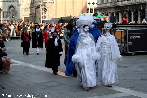White-masked costumed figures parade through St Mark's Square during Venice Carnival