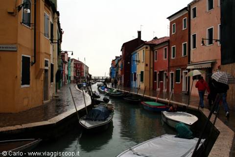 Burano canal with moored boats and colorful houses under rain
