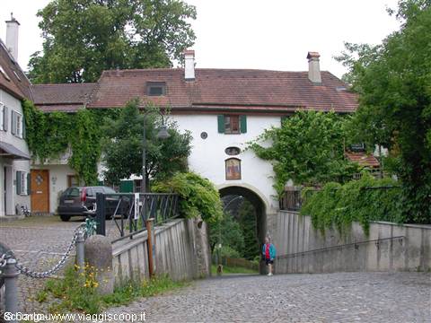 White house with stone arch covered in ivy, cobblestone ramp, cyclist passing