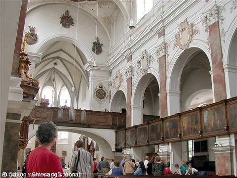 Visitors among wooden pews inside a baroque church with frescoes