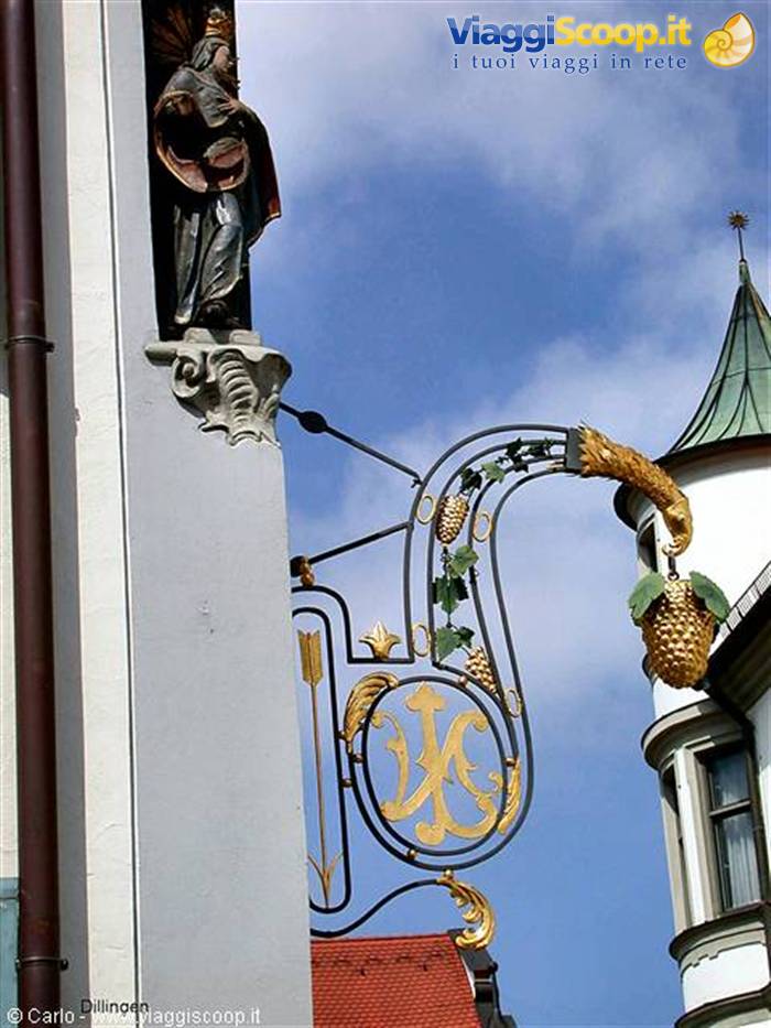 Gilded wrought-iron sign with grape cluster, religious statue, blue sky in Dillingen