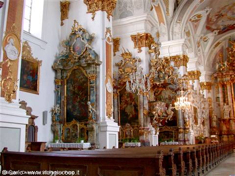 Baroque church interior with gilded altars, crystal chandeliers and wooden pews
