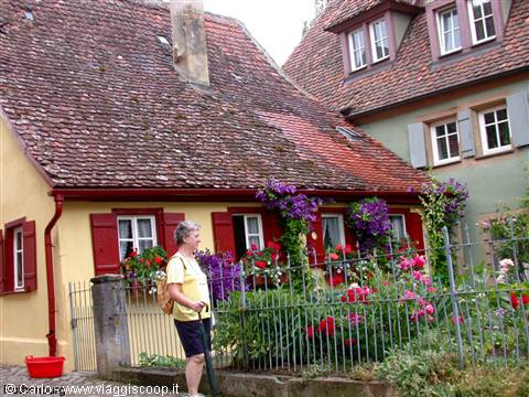 Woman with walking stick beside yellow house, red tiled roofs and clematis