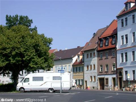 White camper van parked at an intersection of historic red-roofed townhouses