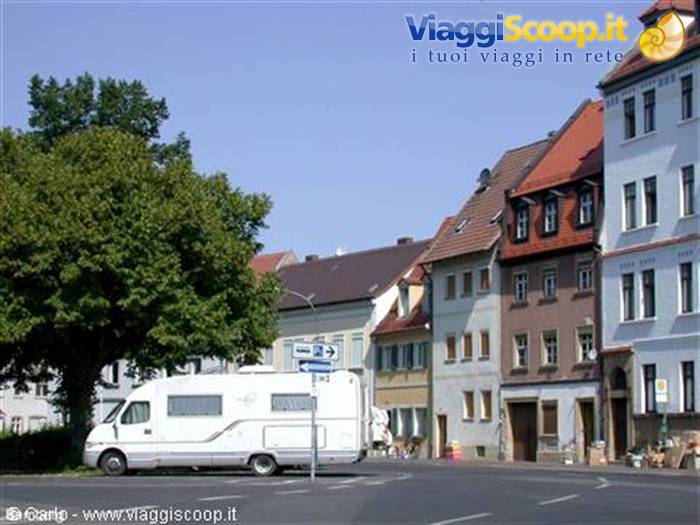White camper van parked at an intersection of historic red-roofed townhouses