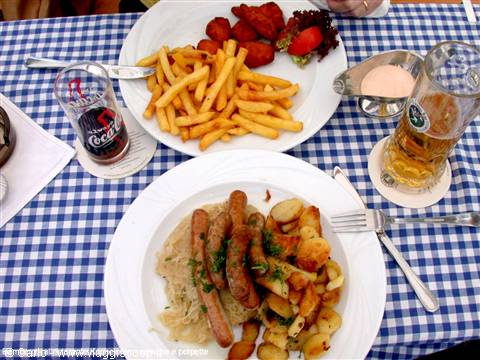 Plates of sausages with sauerkraut, potatoes and fries on checkered tablecloth
