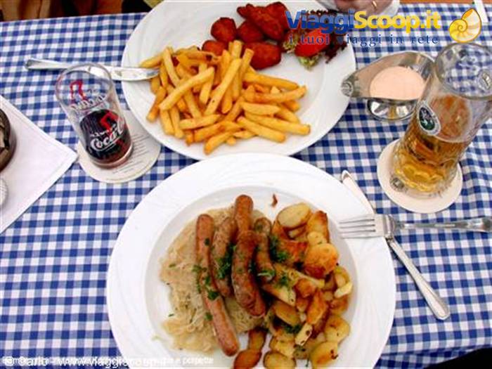 Plates of sausages with sauerkraut, potatoes and fries on checkered tablecloth