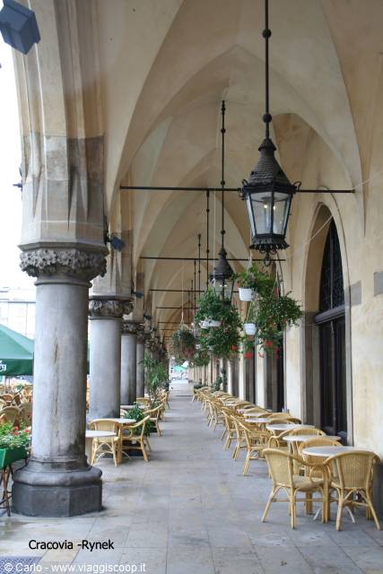 Kraków Rynek arcade with stone columns, hanging lanterns and rattan café chairs