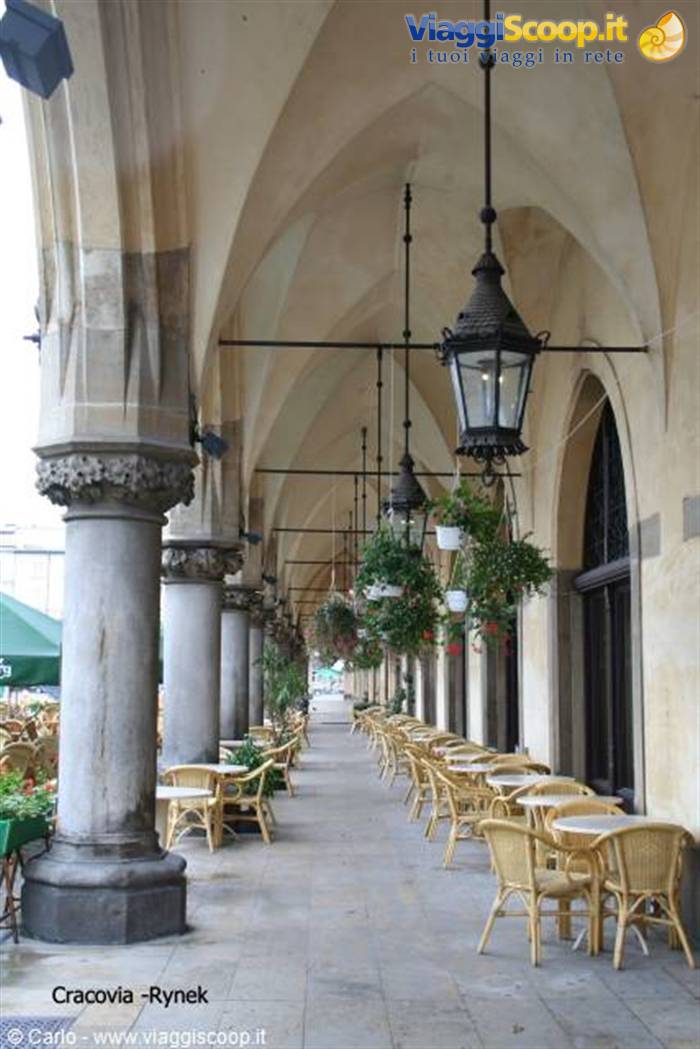 Kraków Rynek arcade with stone columns, hanging lanterns and rattan café chairs