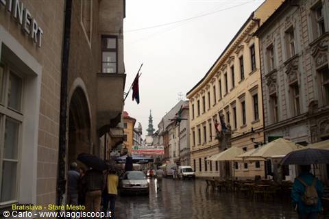 Rain-soaked street with umbrellas and historic buildings in Bratislava