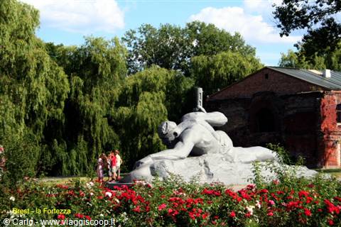 Courage monument at Brest Fortress among red roses and old brick ruins