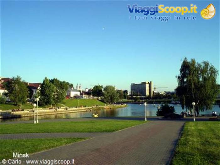 Minsk riverside promenade with paved paths, green lawn and boats on the river